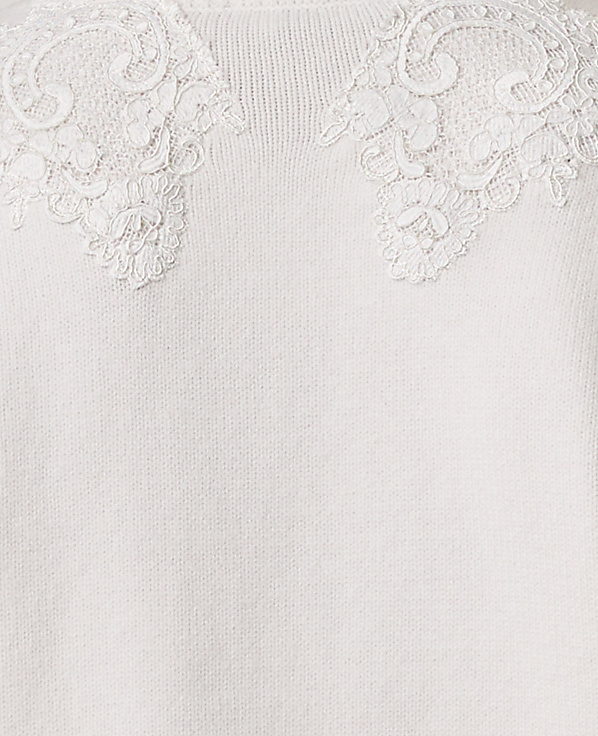 Intricate white lace floral appliqu&eacute;s adorn the neckline of a soft, cream-colored knit fabric.