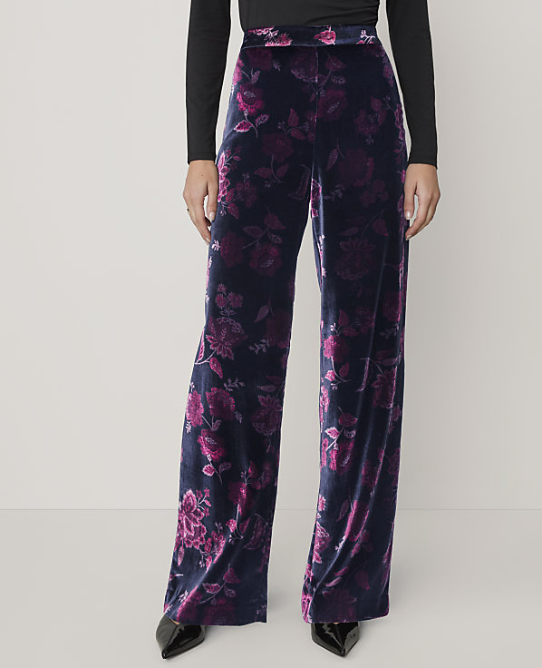 A person wears wide-leg black and purple floral velvet trousers and a black top against a plain light grey background.
