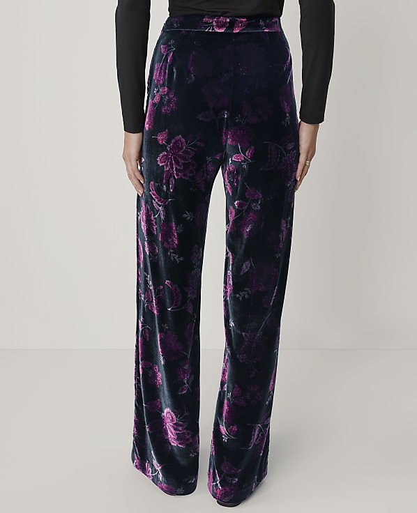 A person wears black long-sleeved top and wide-leg black velvet pants with a purple floral pattern against a plain light gray background.
