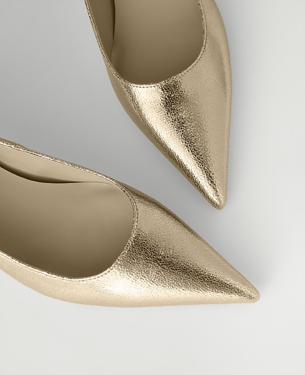 Two metallic rose-gold pointed-toe pumps are positioned diagonally against a plain light gray background.