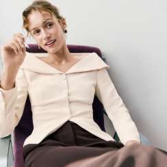 Woman in an ivory wrap-collar jacket seated in a chair