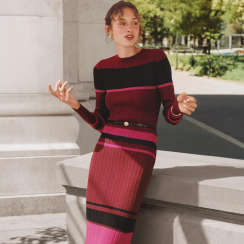 Woman in a burgundy and pink striped sweater and pleated skirt