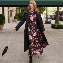 Woman in a floral midi dress and long black coat on a city sidewalk