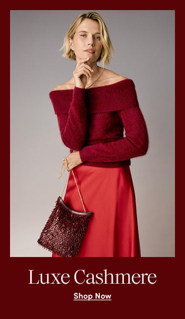 A woman in a burgundy off-the-shoulder sweater and red satin skirt against a grey background.