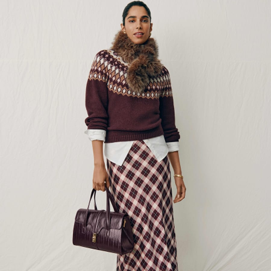 Woman in a Fair Isle sweater with a faux fur collar, plaid midi skirt and burgundy bag