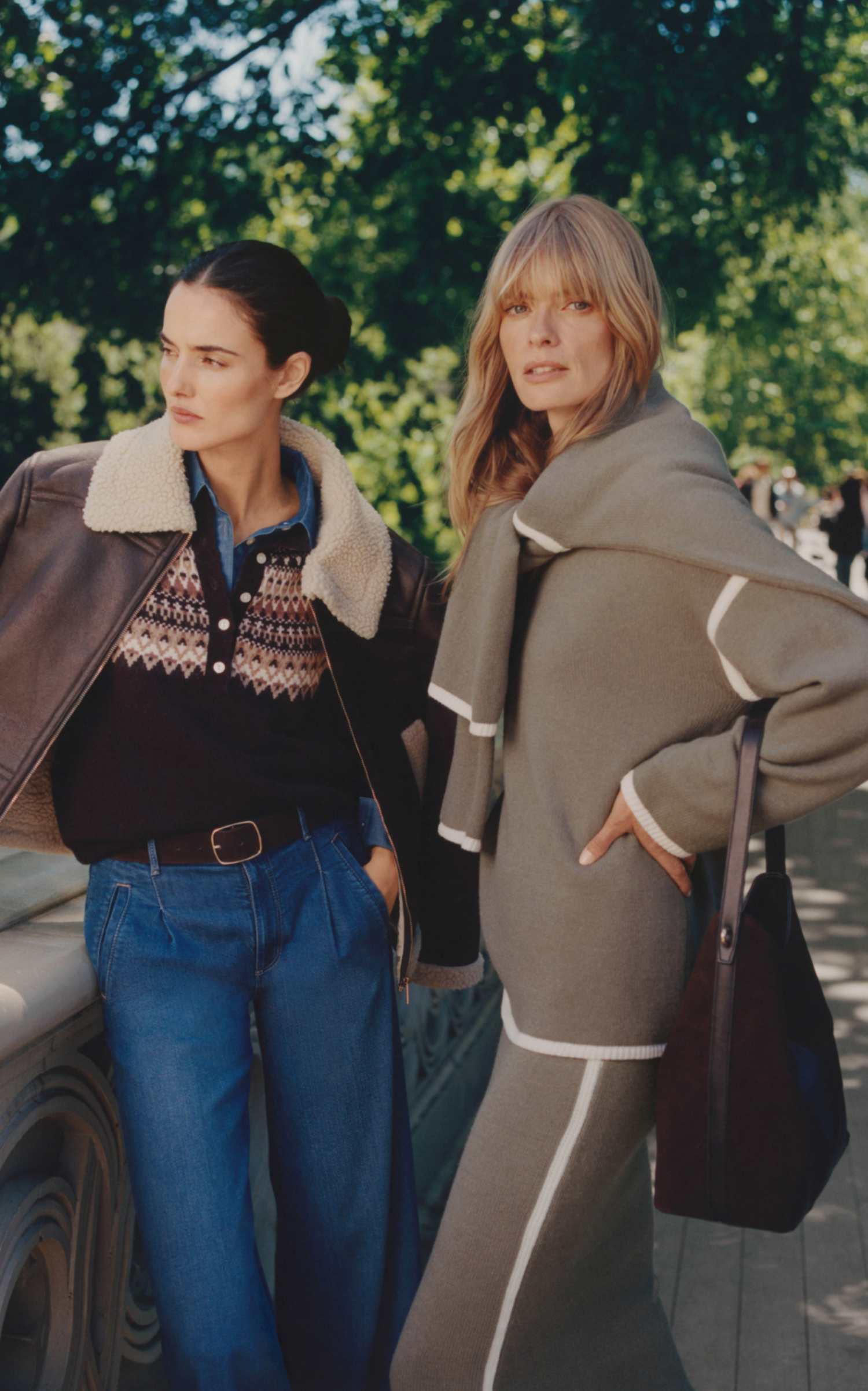 Two women by a lake in the park, one in a shearling-collar leather jacket and Fair Isle sweater, one in a grey knit set with a draped scarf